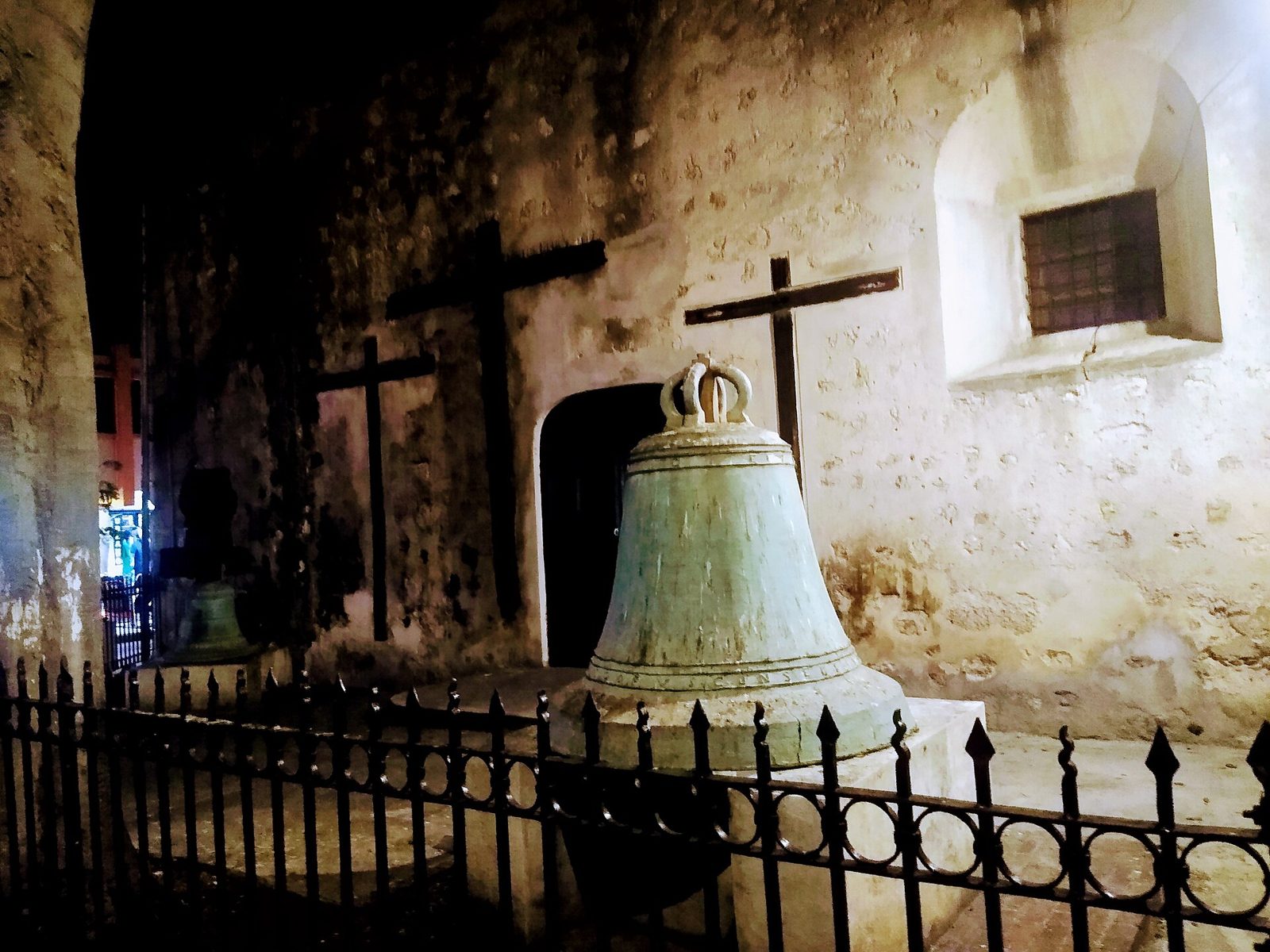 Bronze bells and crosses outside the side door of Mérida Cathedral at night