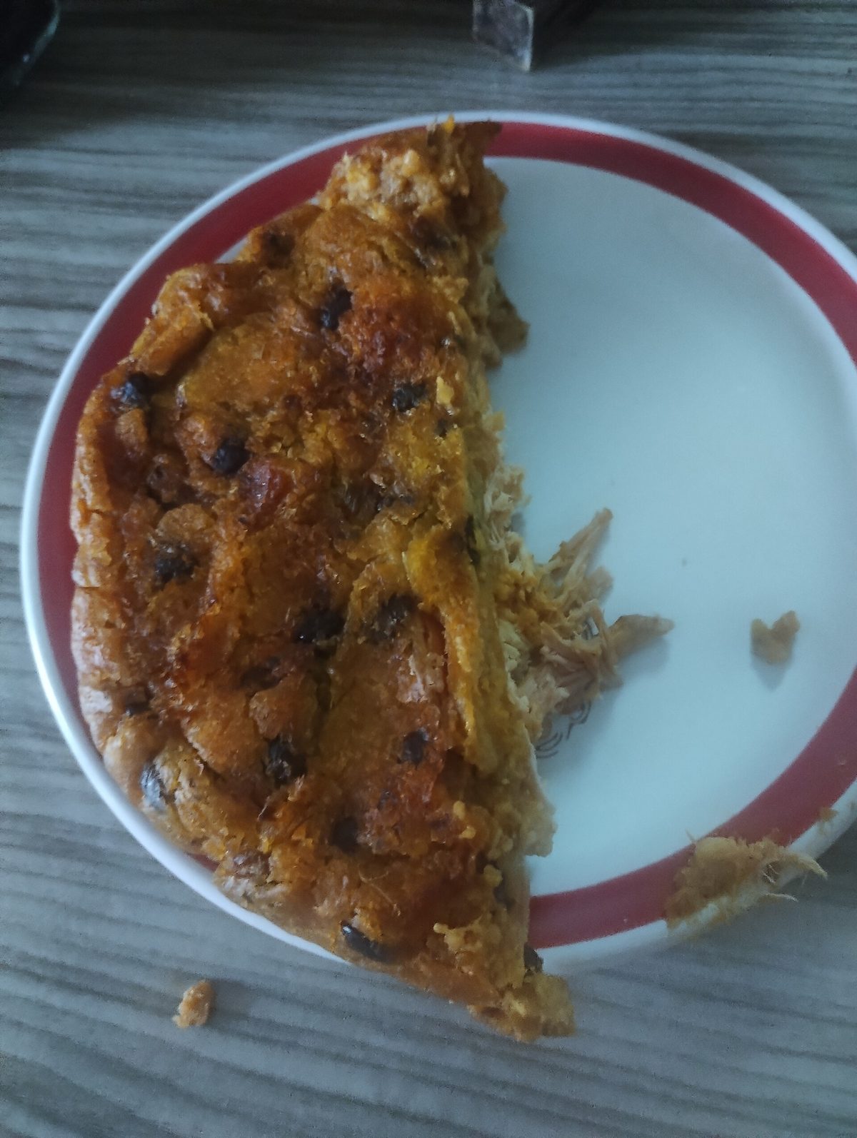 Une part de pib à la croûte dorée, farce de viande effilochée visible, dans une assiette blanche bordée de rouge
