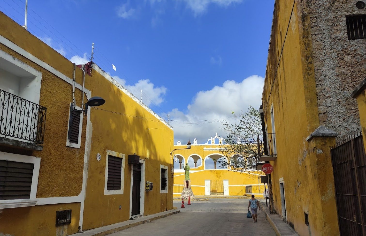 Maisons coloniales jaunes le long d'une rue tranquille d'Izamal, avec les arcades du couvent au bout