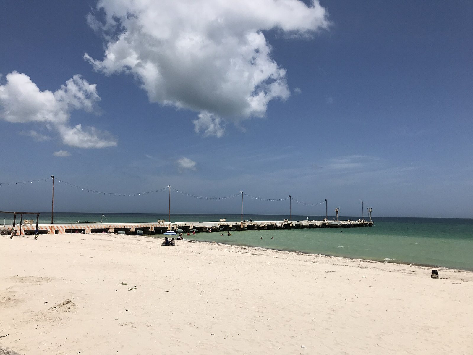 Wide white-sand beach at Telchac Puerto with the long wooden pier running into shallow green water