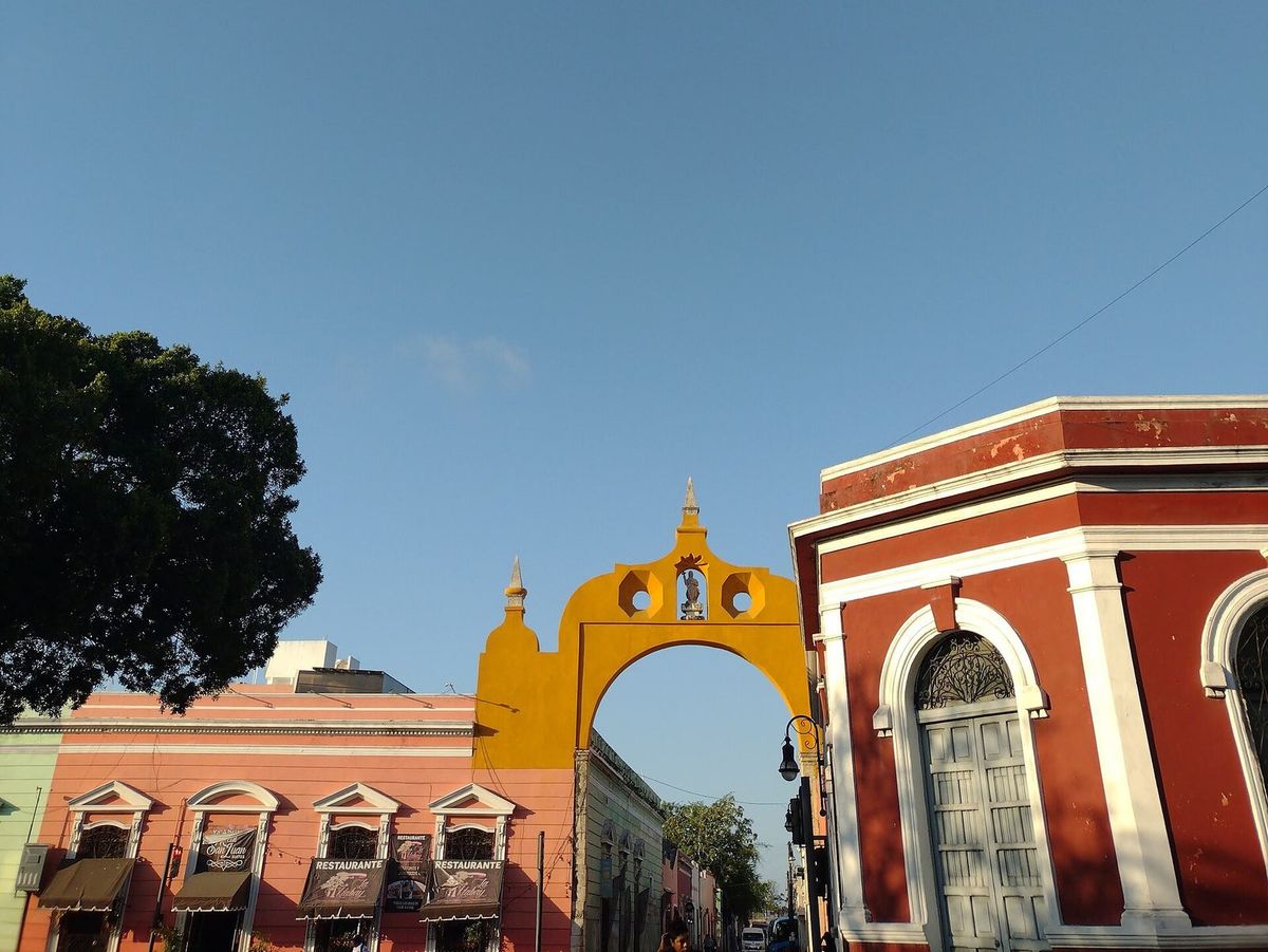 L'Arco de San Juan, jaune et colonial, enjambant une rue entre des maisons rouges et roses sous un ciel bleu