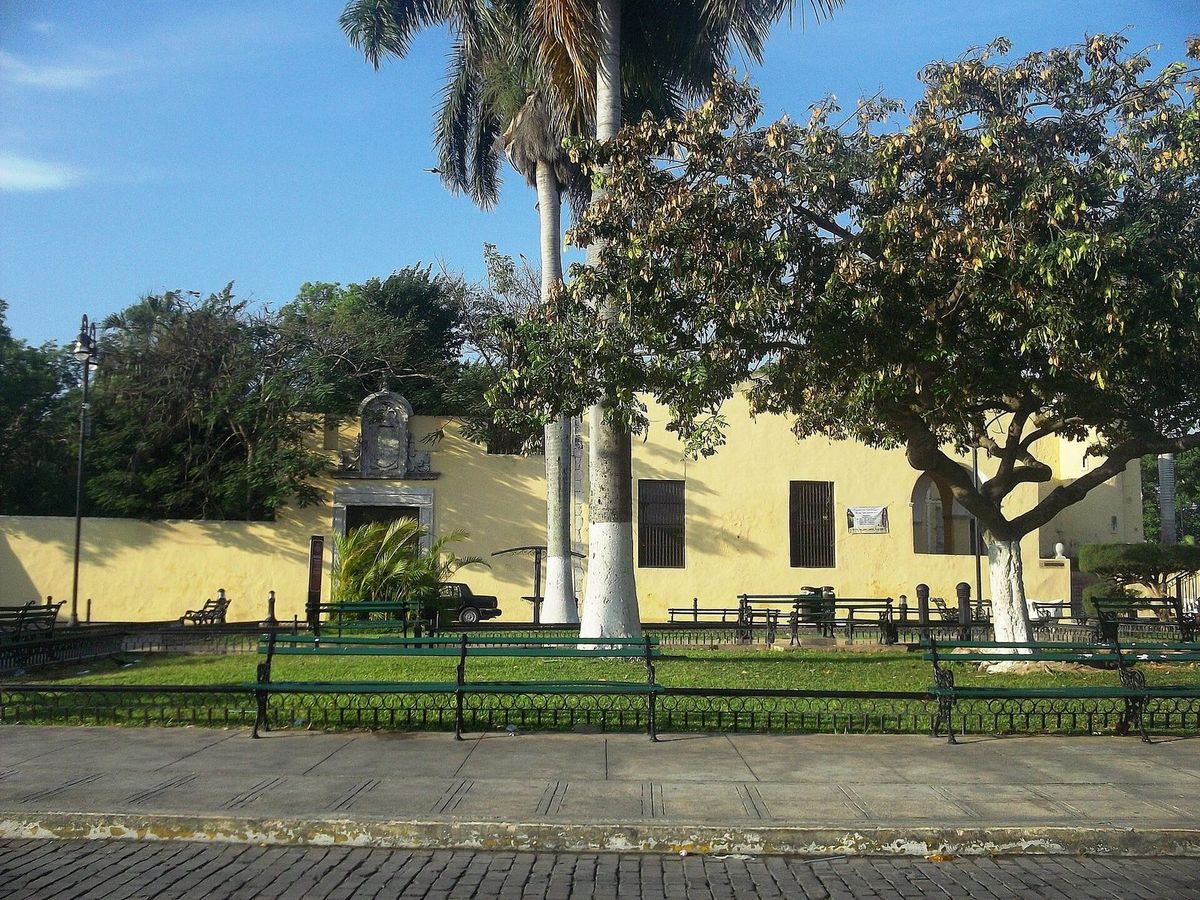 La petite chapelle jaune de l'Ermita de Santa Isabel derrière une pelouse clôturée, avec palmiers et arbres