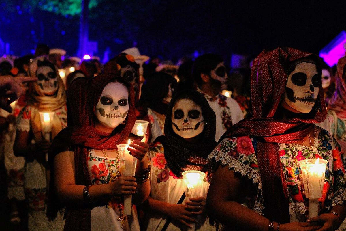 Femmes en huipil brodé et châle rouge, le visage peint en tête de mort, tenant des bougies allumées la nuit pendant le Paseo de las Ánimas à Mérida