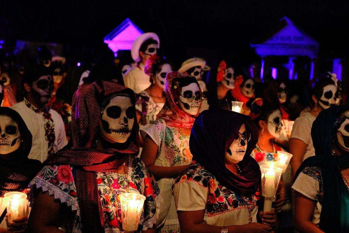 Rangées de participants du Paseo en huipil, visage peint en tête de mort et bougie à la main, sous une lumière violette